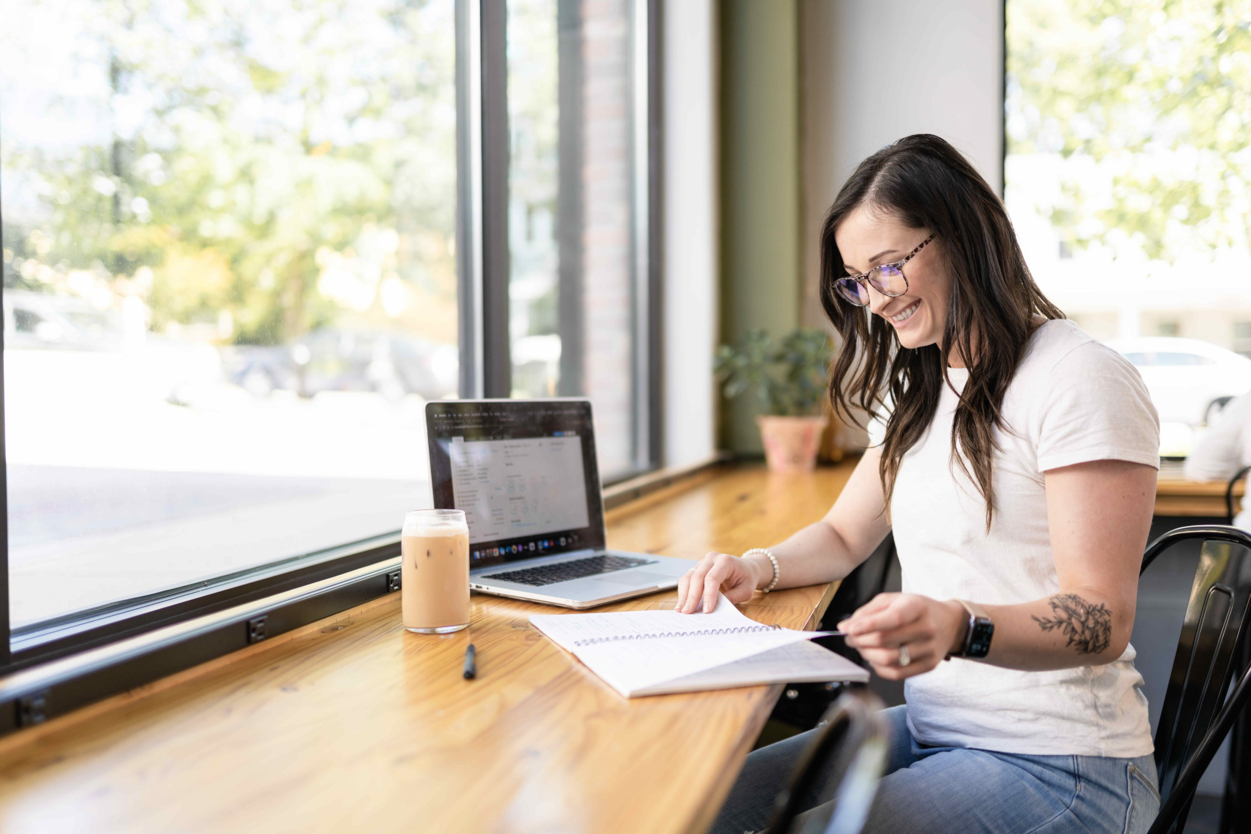 A smiling woman working from a brightly lit coffee shop